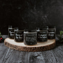 Load image into Gallery viewer, From left to right, the flourishing forest candle, siren of the sea candle, emerald hearth candle, enchantress of the inferno candle, and bewitching breeze candle displayed on a wood slat with a back background.