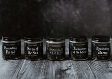 Load image into Gallery viewer, The Elemental Mini Bundle Set which includes (from left to right) the Flourishing Forest candle, Siren of the Sea candle, Emerald Hearth candle, Enchantress of the Inferno candle, and Bewitching Breeze candle all displayed on wood with a black background.