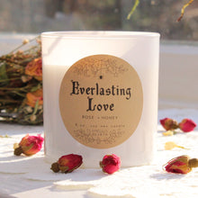 Load image into Gallery viewer, The white Everlasting Love candle with rosebuds around it photographed in the sunlight.  This candle is by Emerald Hearth Creations.