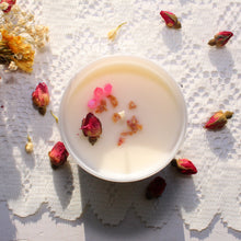 Load image into Gallery viewer, The top of the Everlasting Love candle by Emerald Hearth. The candle has rosebuds and pink quartz on top. The candle is atop a white lace background which has more rosebuds around it.