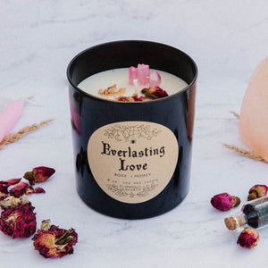 A side view of the Everlasting Love candle by Emerald Hearth Creations. The candle is on a white backdrop and is surrounded by rosebuds.