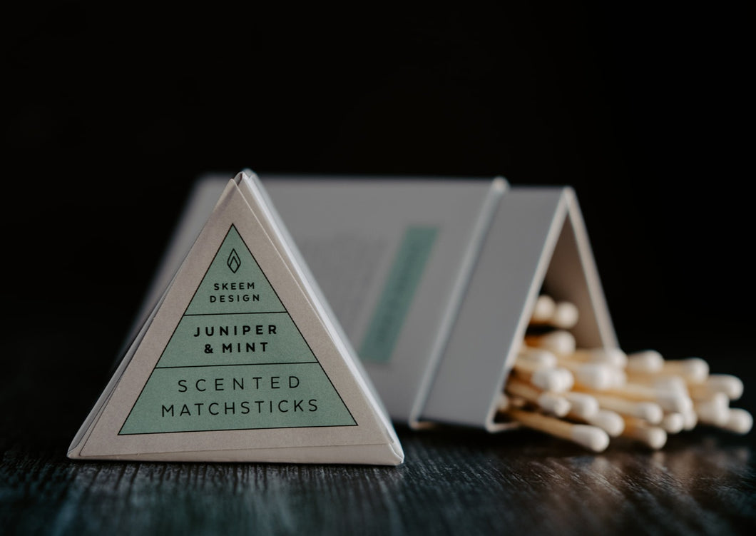Image of Juniper & Mint scented match sticks.  The lid of the triangle packaging is in the foreground and in focus.  The background is of the matches which is out of focus.