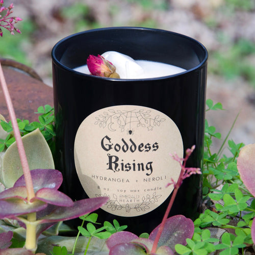 Image of the Emerald Hearth Goddess Rising Candle in black.  The candle is in a garden.  The rose bud on top is visible.