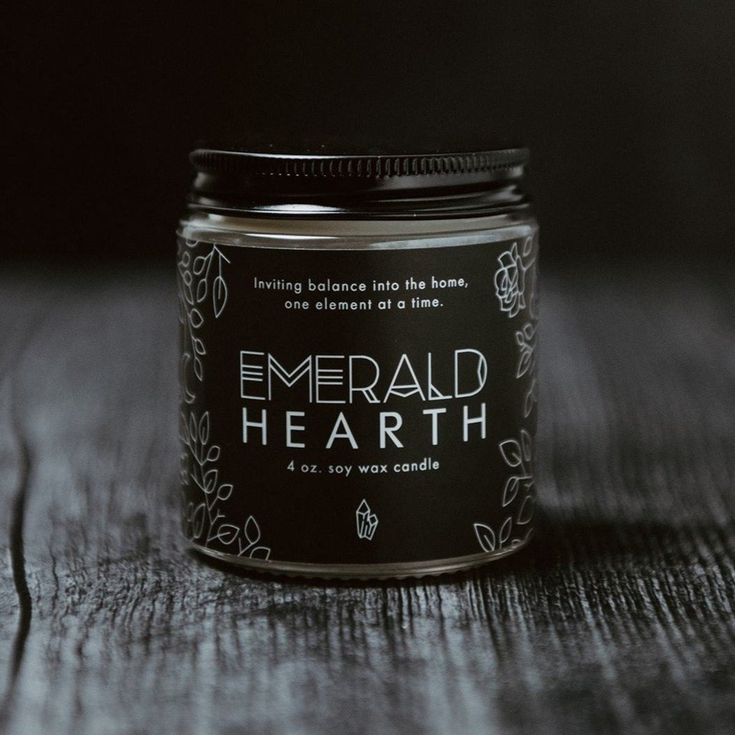 The mini Emerald Hearth original candle photographed on wood with a black background.