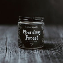 Laden Sie das Bild in den Galerie-Viewer, The mini 4oz version of the Emerald Hearth candle, Flourishing Forest.  The candle is photographed on wood with a black background.