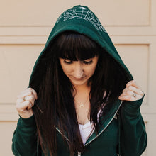Load image into Gallery viewer, The founder of Emerald Hearth, Brittney wearing the Green Emerald Hearth hoodie and looking down.