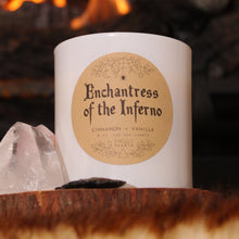 Load image into Gallery viewer, The Enchantress of the Inferno candle by Emerald Hearth in white, photographed next to a piece of pink quartz.  There is fire in the background.