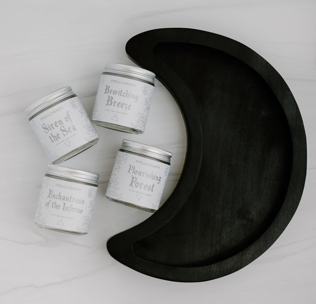Wooden crescent moon tray displayed with four candles all sold by emerald hearth.  The wooden tray is a crescent moon shape in a dark wood. All five products are on a white background.