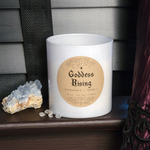 Image of the Emerald Hearth Goddess Rising Candle in White.  The candle is on a bookshelf with a crystal next to it.