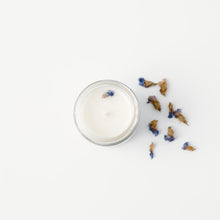 Load image into Gallery viewer, The mini version of the Slumbers End candle by Emerald Hearth Creations.  This ritual equinox candle is photographed against a white background and surrounded byviolet Forget Me Not flowers.  The candle&#39;s packaging is white with gold accents.